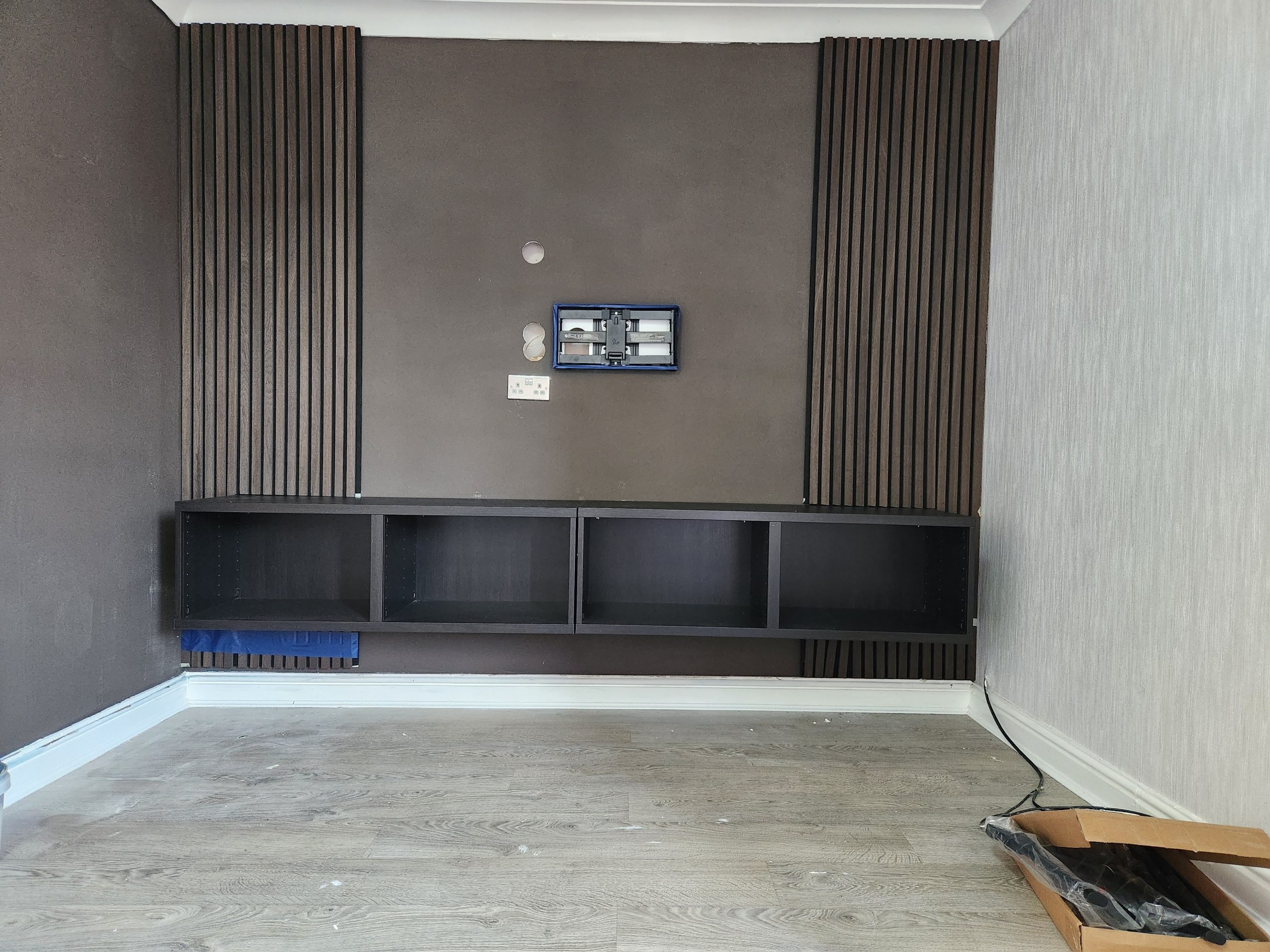 Media wall with dark slatted wood panels either side of a textured feature wall and a floating shelf unit