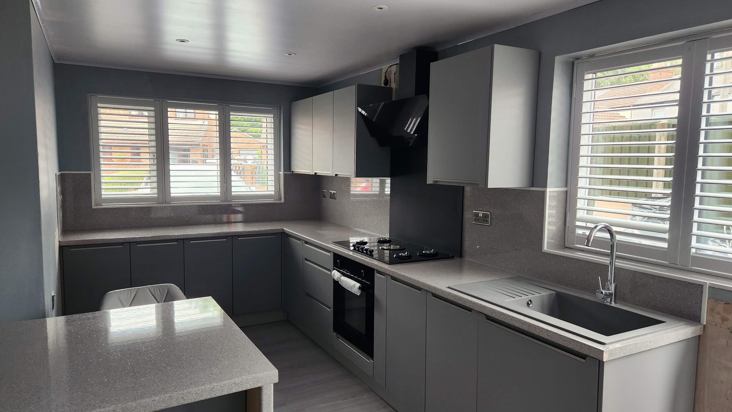 Finished kitchen with dark grey handleless units, grey stone-effect worktops, black extractor and white shutters