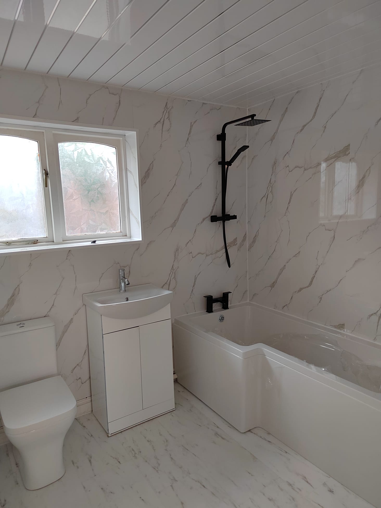 Refitted bathroom with marble-effect panelling, white suite and black shower fittings