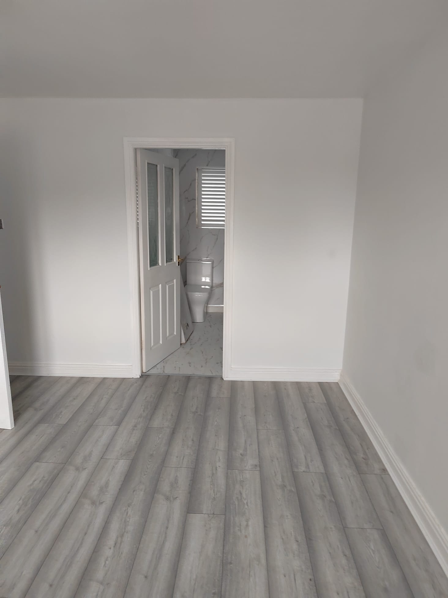 Refurbished room with white walls and grey flooring, looking through to the new bathroom