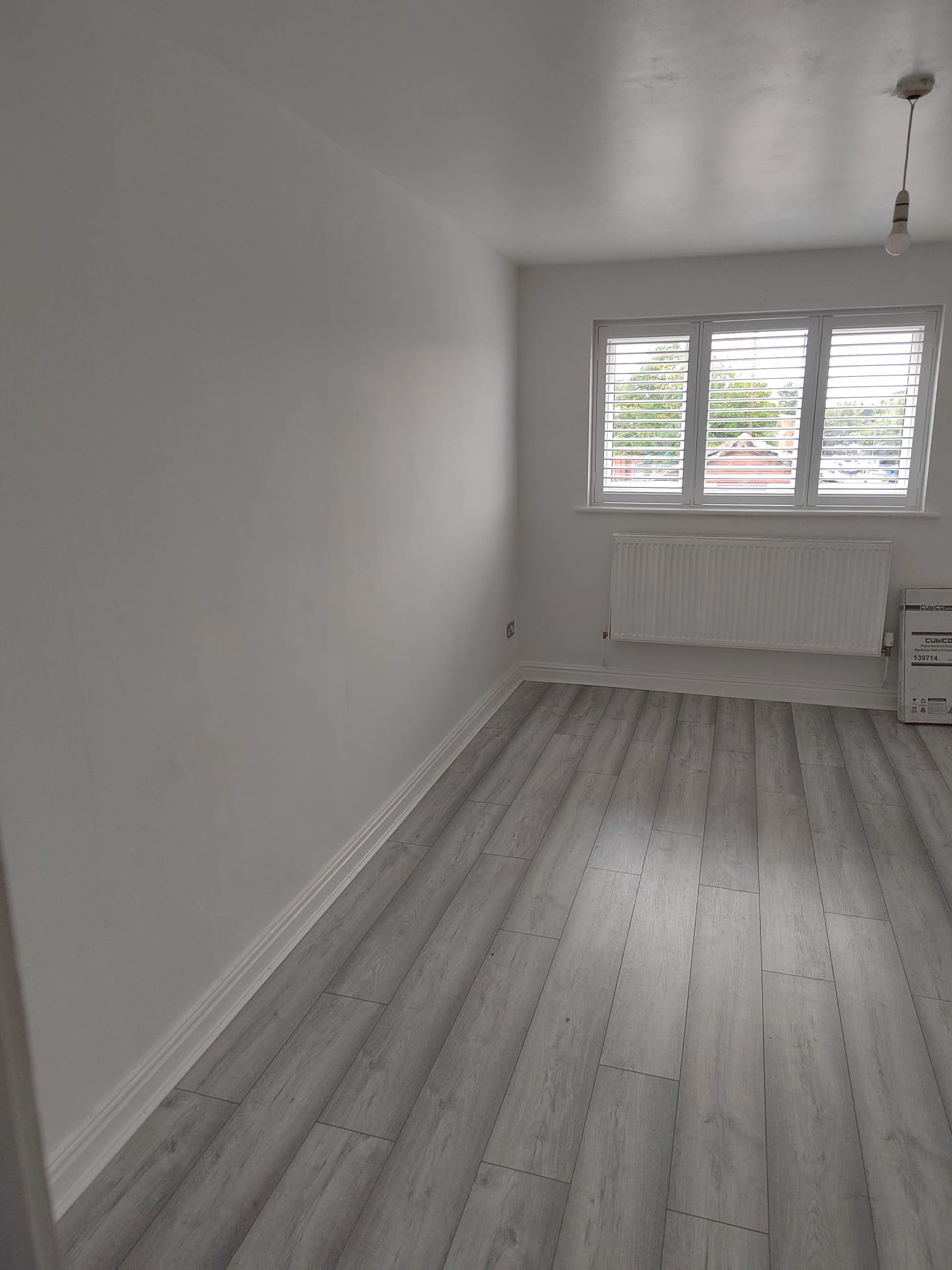 Freshly decorated room with white walls, grey wood-effect flooring and a new radiator under the window